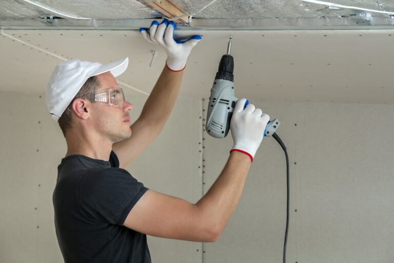 Young man in goggles fixing drywall suspended ceiling to metal frame
